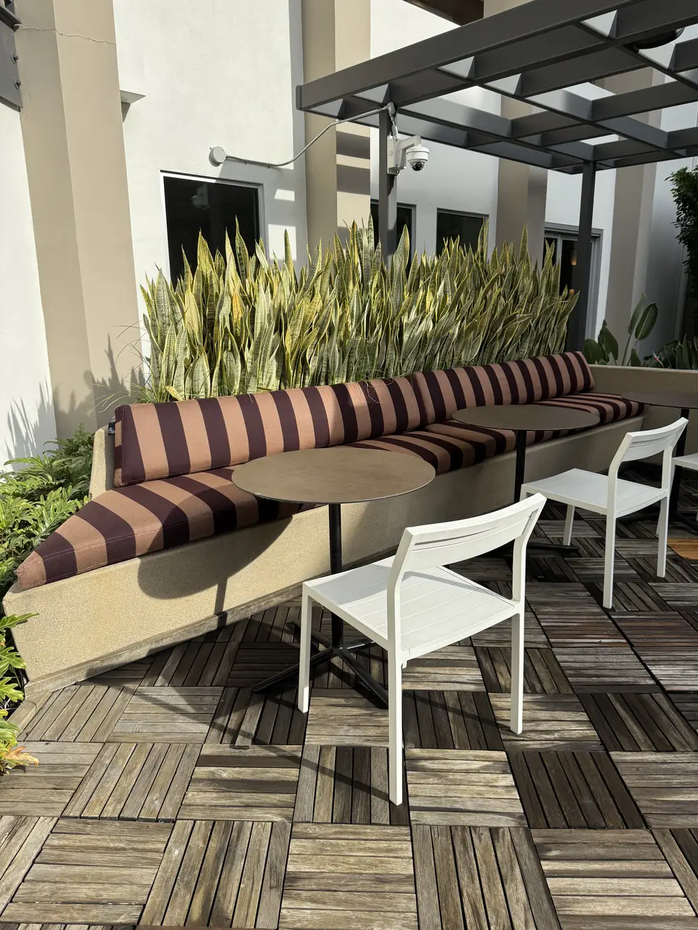 Long built-in banquette with striped outdoor cushions along a planter wall, with cafe tables, at The Brio, Glendale