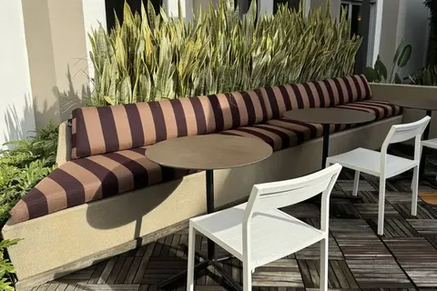 Long built-in banquette with striped outdoor cushions along a planter wall, with cafe tables, at The Brio, Glendale